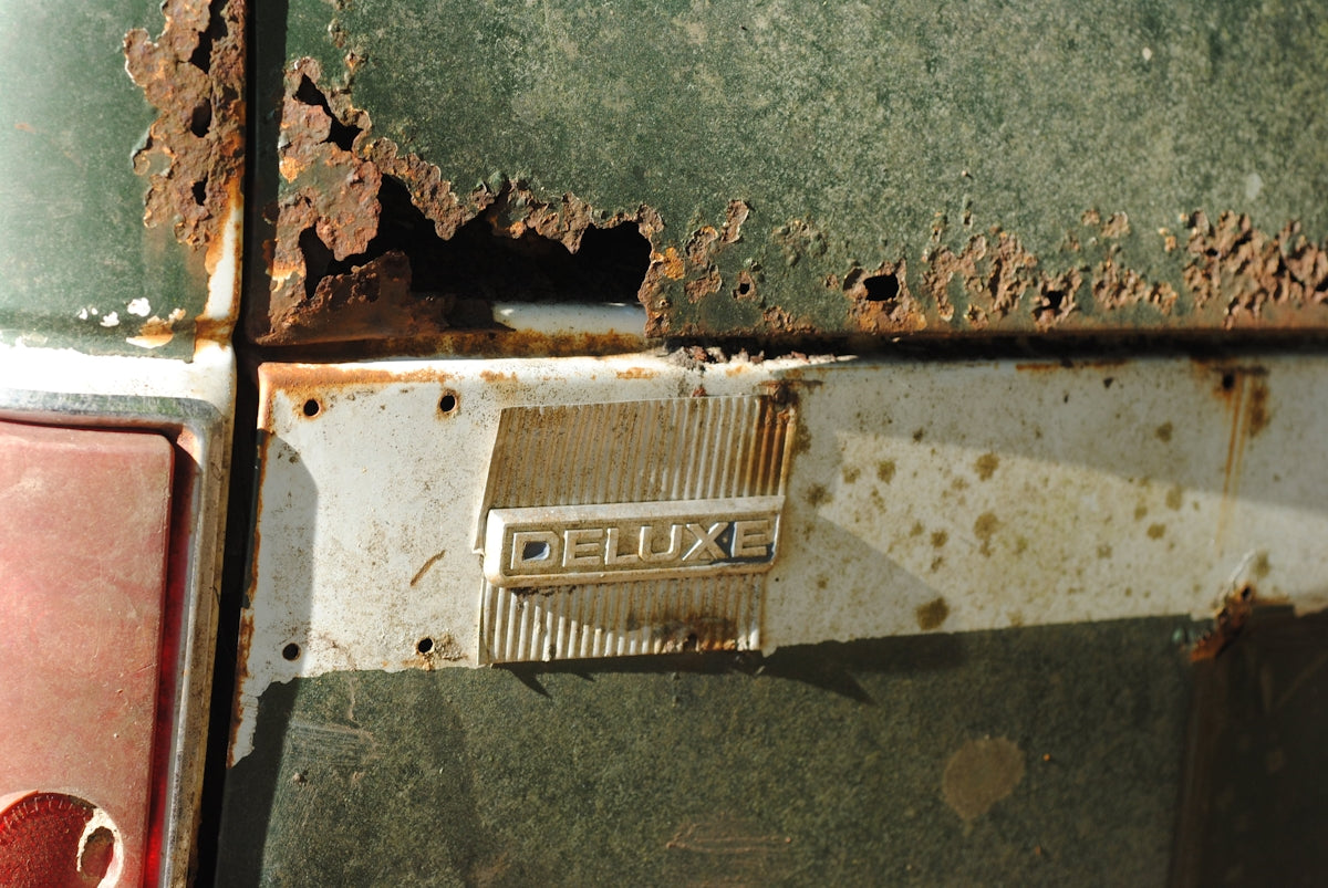 Rusted vintage car with deluxe emblem.