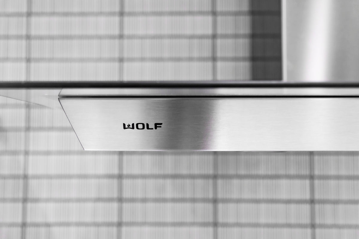 Stainless steel range hood with wolf logo.